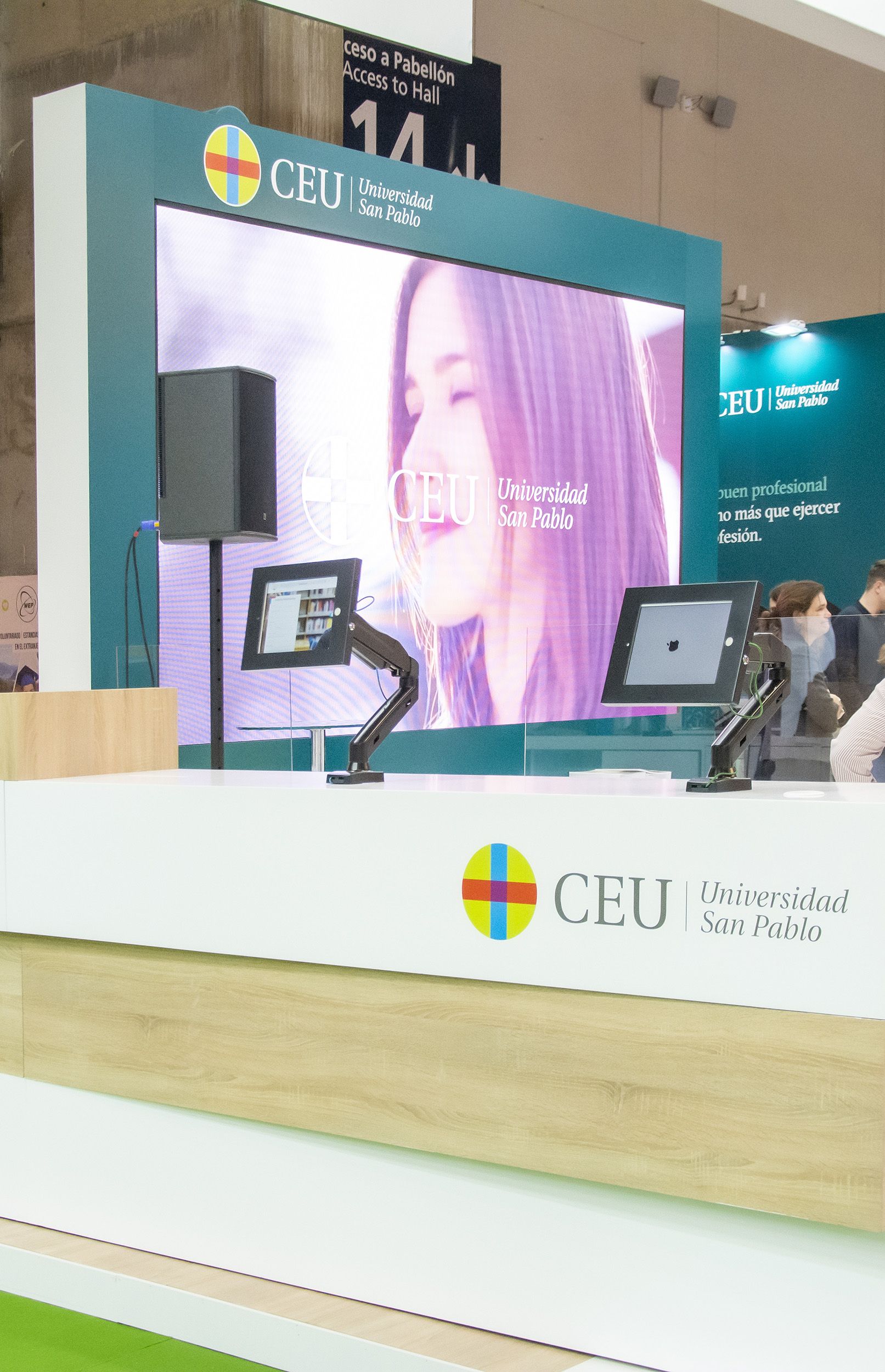 Detail of university exhibition stand in Madrid with service counters, tablets for visitors, and LED digital screen in the background