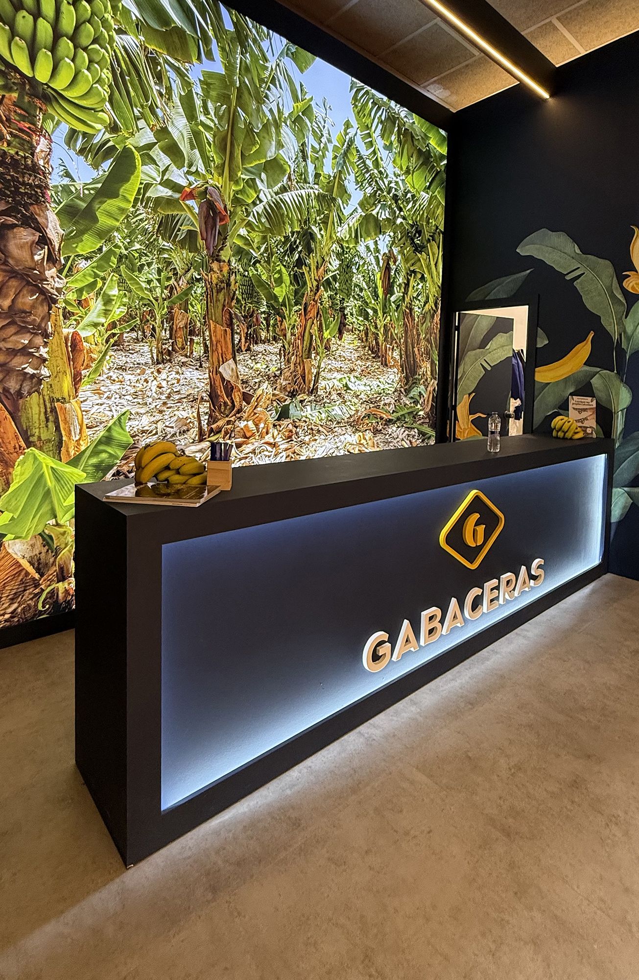 Interior counter of an inline exhibition stand in Madrid with perimeter LED lighting, 3D logo, and tropical backlit graphic background